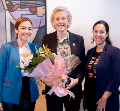 Three smiling women pose with flowers