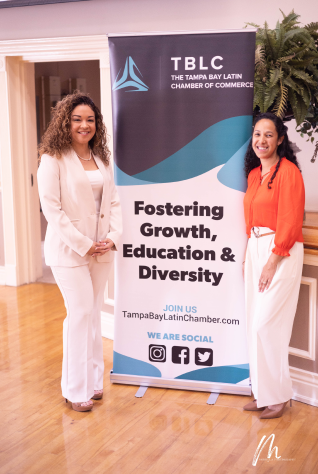 Women smile next to poster saying, "Fostering Growth, Education & Diversity"