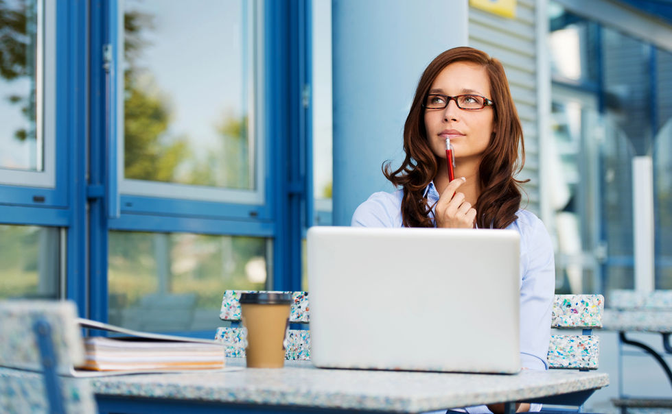 Writer thinking at coffee shop with pen and laptop